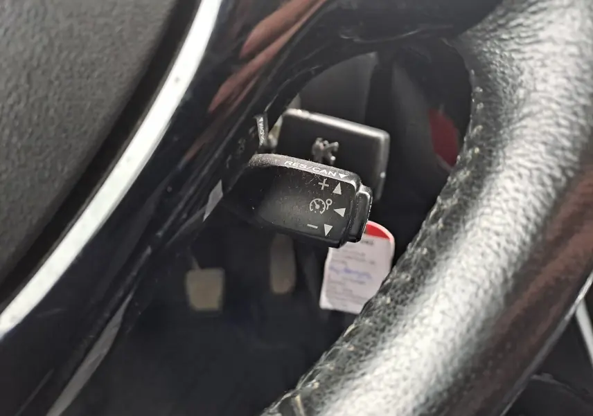 Gros plan sur le levier de régulateur de vitesse derrière le volant noir d'une Peugeot 108 bleu, intérieur visible.