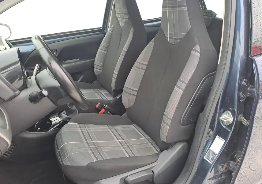 Vue intérieure côté conducteur de la Peugeot 108 bleue, mettant en valeur les sièges tissu à motifs gris et noirs.