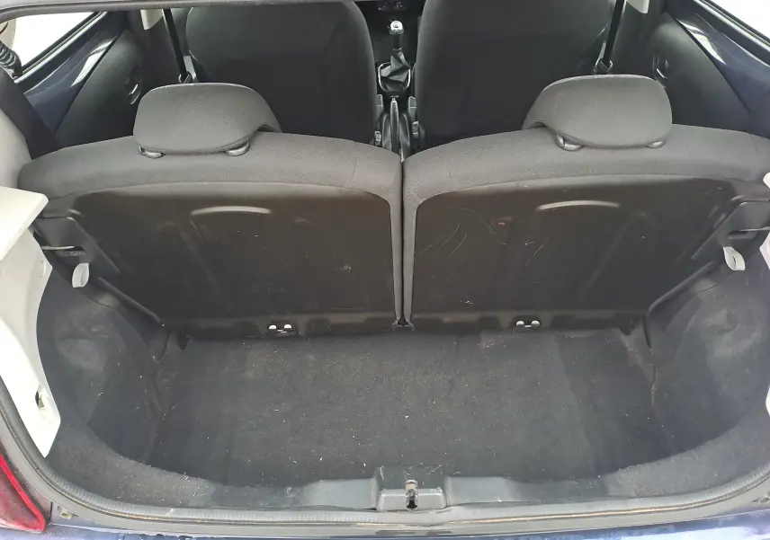 Vue du coffre ouvert d'une Peugeot 108 bleu 2016, montrant les dossiers arrière rabattus et l'espace de chargement vide.