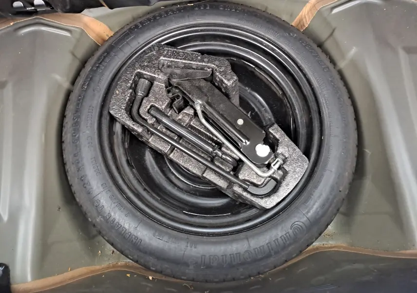 Gros plan sur la roue de secours noire et les outils de bord dans le coffre d'une Peugeot 108 bleue de 2016.