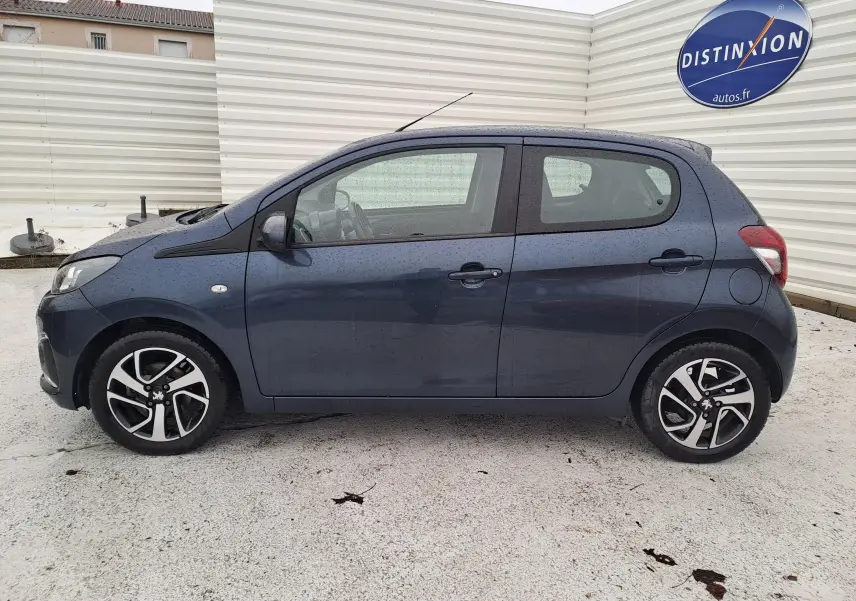 Profil côté gauche d'une Peugeot 108 bleu 5 portes avec jantes alliage bicolores, sous une légère pluie.