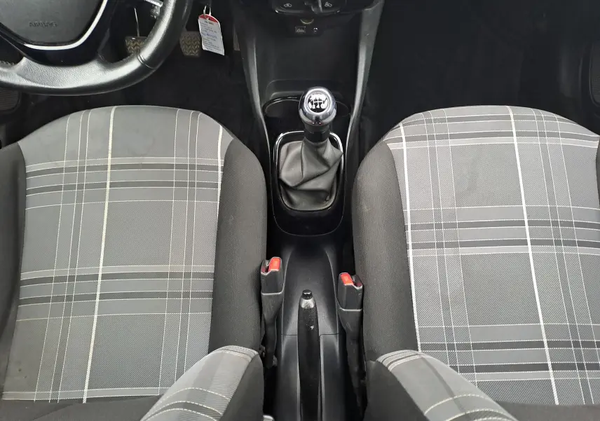 Vue intérieure centrée sur la console centrale et la boîte manuelle de la Peugeot 108 avec sièges avant gris à motif à carreaux.