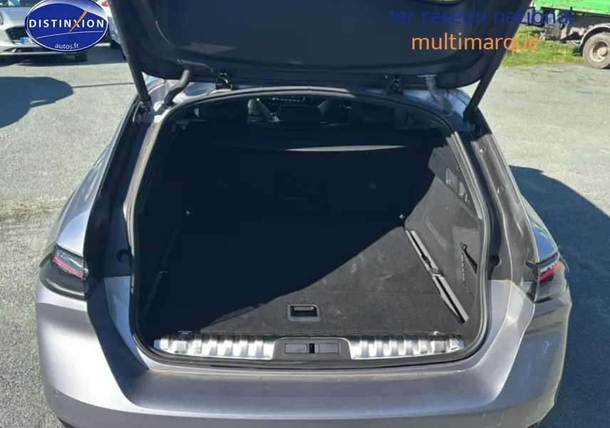 Coffre ouvert vu de l'arrière d'une Peugeot 508 SW Hybrid 225 gris artense, avec hayon relevé et espace de chargement vide.