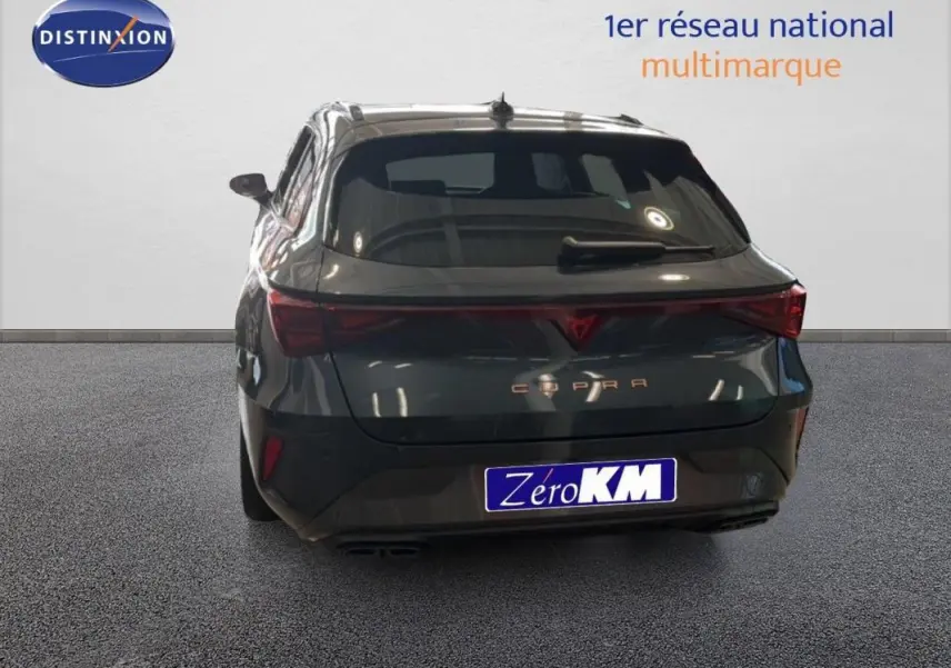 Vue arrière d'une CUPRA Leon ST gris avec barres de toit et feux arrière allumés, en intérieur showroom.