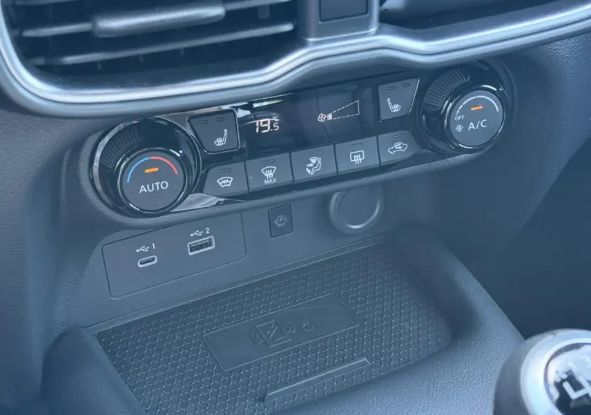 Détail de la console centrale du Nissan Juke 2025, montrant les commandes de climatisation et les ports USB avec recharge sans fil.