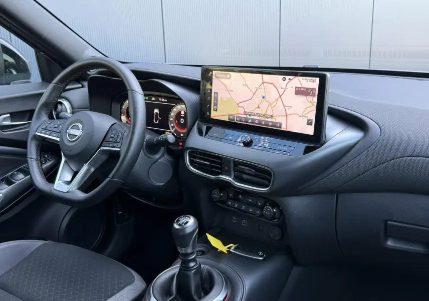 Vue intérieure côté conducteur du Nissan Juke 2025, tableau de bord noir avec écran tactile GPS et levier de vitesse manuel.