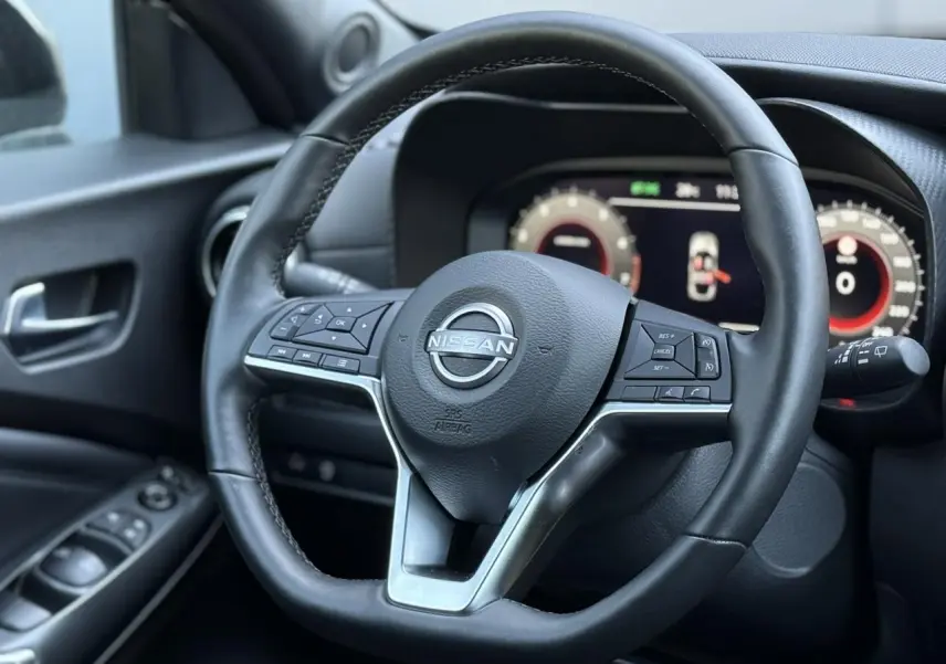 Gros plan sur le volant en cuir noir du Nissan Juke 2025 avec commandes intégrées et tableau de bord digital en arrière-plan.