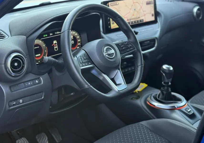 Vue intérieure côté conducteur du Nissan Juke 2025 bleu magnétique, volant cuir, écran tactile GPS et boîte manuelle.