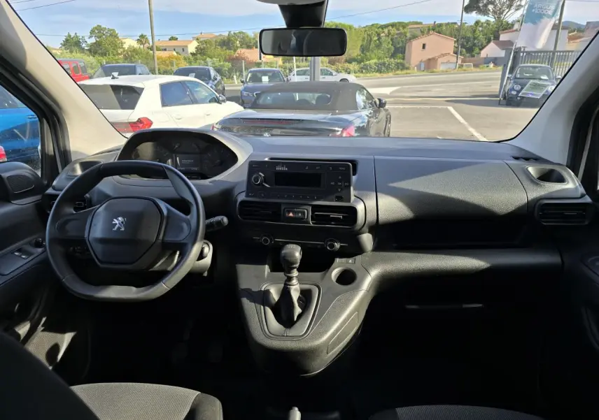 Vue intérieure avant du Peugeot Rifter 1.5 BlueHDi blanc, montrant le volant, tableau de bord et levier de vitesses manuel.