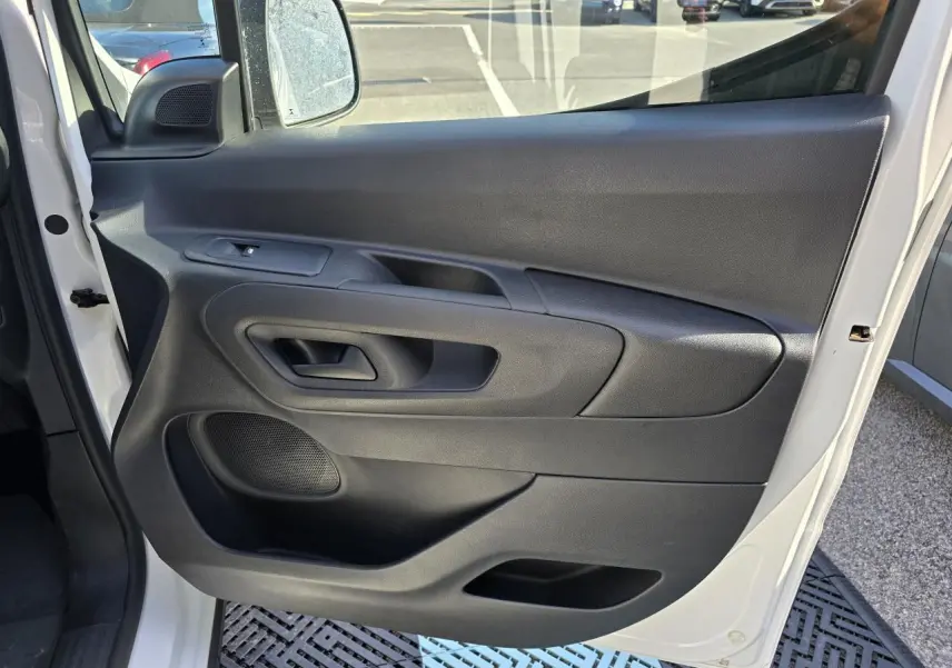Vue de la porte avant gauche ouverte d’un Peugeot Rifter blanc banquise, avec panneau intérieur noir et commande de lève-vitre.
