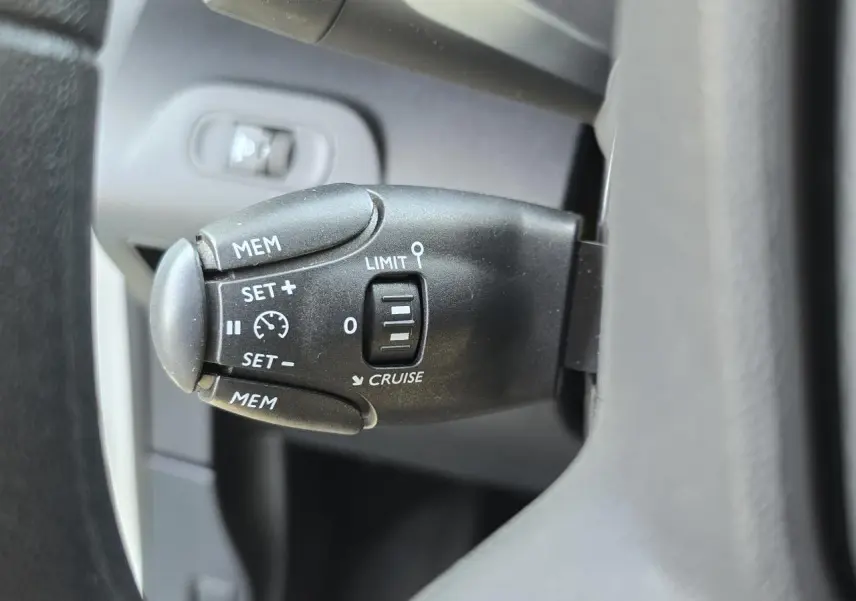 Gros plan sur la commande de régulateur de vitesse noire à gauche du volant du Peugeot Rifter blanc banquise 2021.
