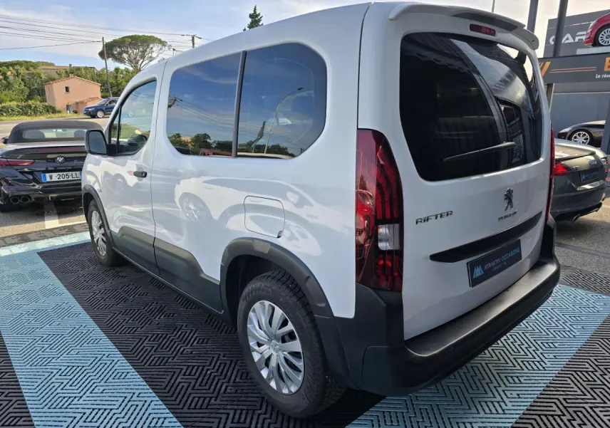 Vue 3/4 arrière droite d'un Peugeot Rifter blanc banquise avec vitres teintées et jantes tôle 16 pouces.
