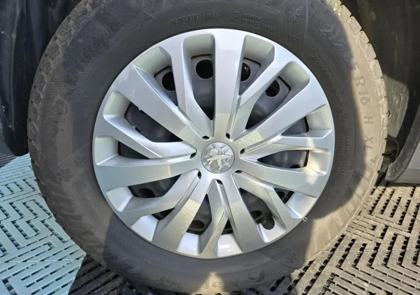 Gros plan sur la roue avant droite du Peugeot Rifter blanc Banquise avec enjoliveur argenté et logo lion central.