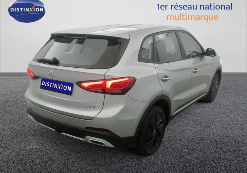 Vue 3/4 arrière droite du SUV MG ZS 1.5 L Hybrid+ 2026 en Cosmic Silver avec feux arrière allumés.