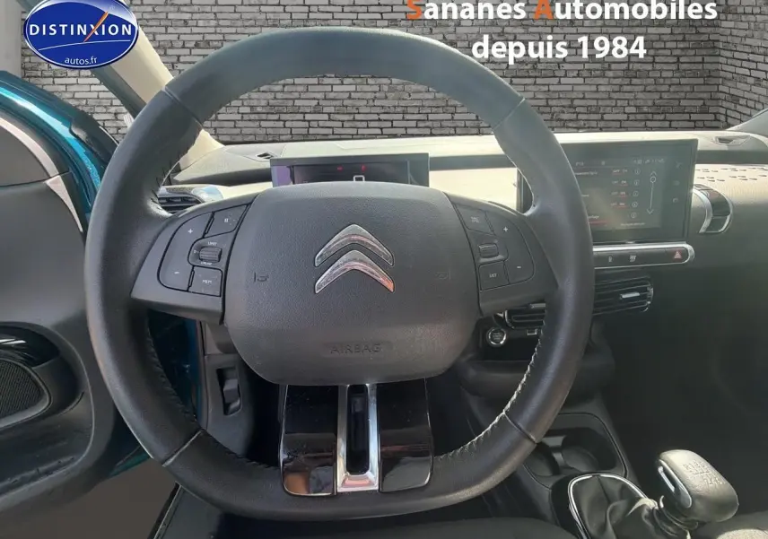 Vue intérieure centrée sur le volant cuir de la Citroën C4 Cactus bleu métal, avec tableau de bord et levier de vitesses manuel visibles.