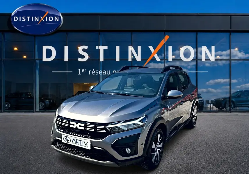 Dacia Sandero Stepway gris schiste vue 3/4 avant droit, avec barres de toit et jantes distinctives.