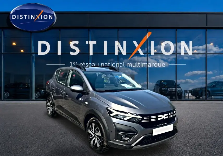 Dacia Sandero Stepway gris schiste vue 3/4 avant droit avec barres de toit et jantes distinctives.