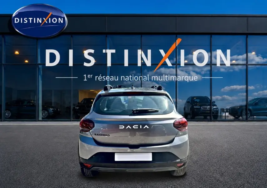 Vue arrière d'une Dacia Sandero gris schiste garée devant une vitrine avec logo Distinxion.