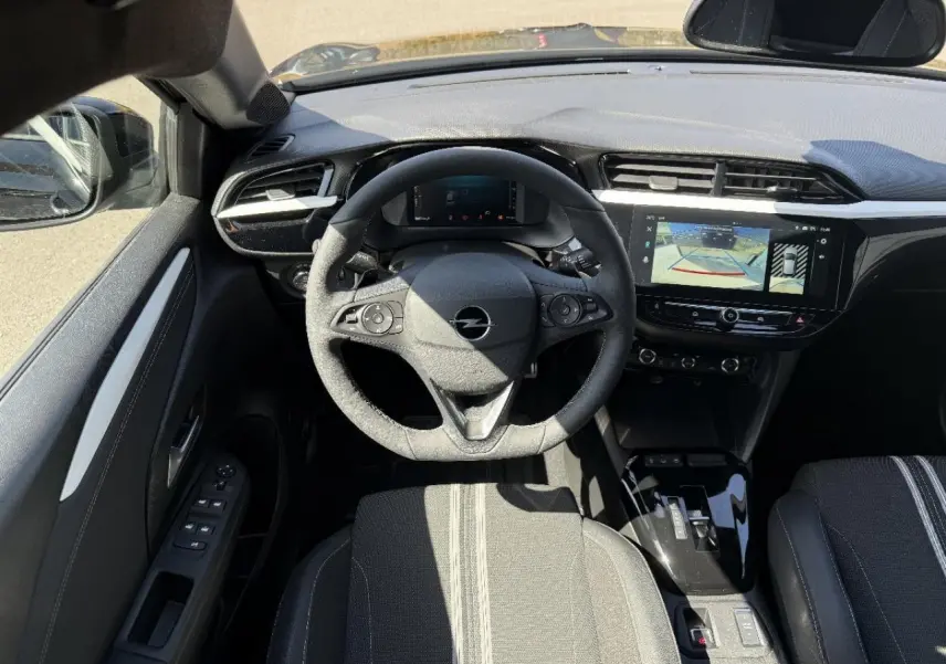 Vue intérieure centrée sur le volant et tableau de bord de l’Opel Corsa noir perla nera avec écran tactile et caméra de recul.