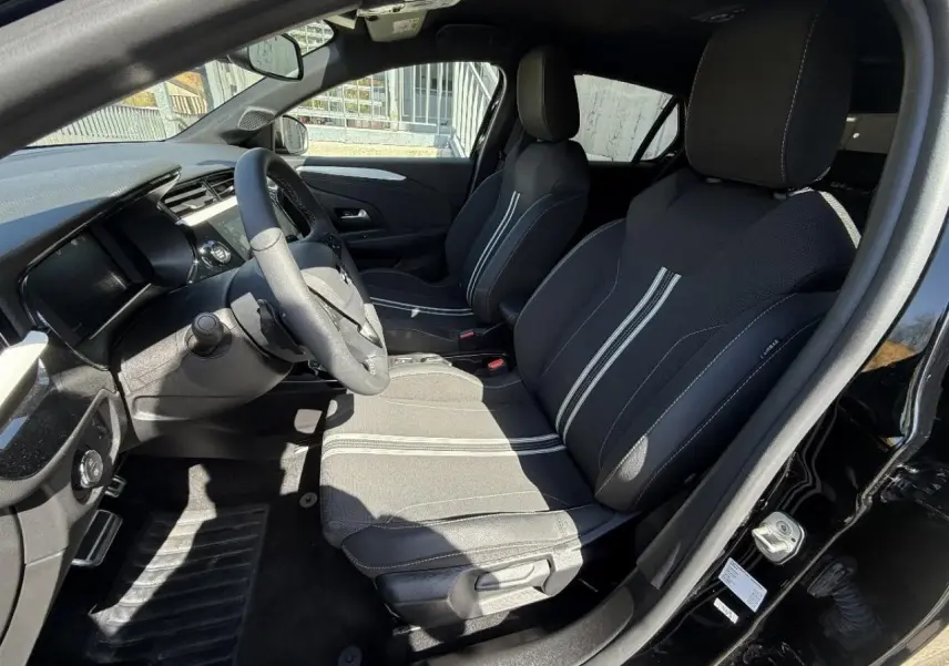 Vue intérieure côté conducteur de l’Opel Corsa 1,2 Hybrid 2025 noir perla nera, sièges tissu avec bandes blanches centrales.