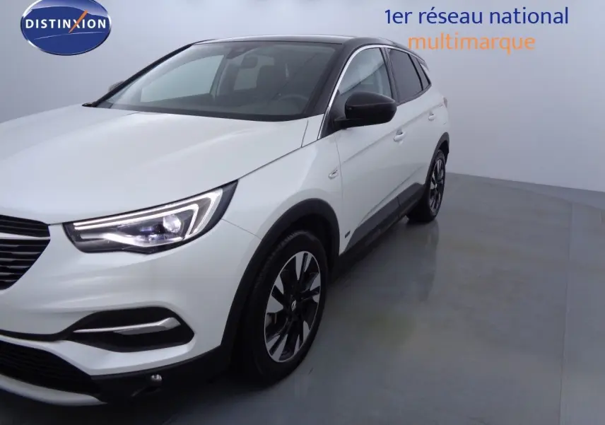 Gros plan sur la roue avant gauche du SUV Opel Grandland X blanc nacré avec badge Hybrid 4 sur la carrosserie.