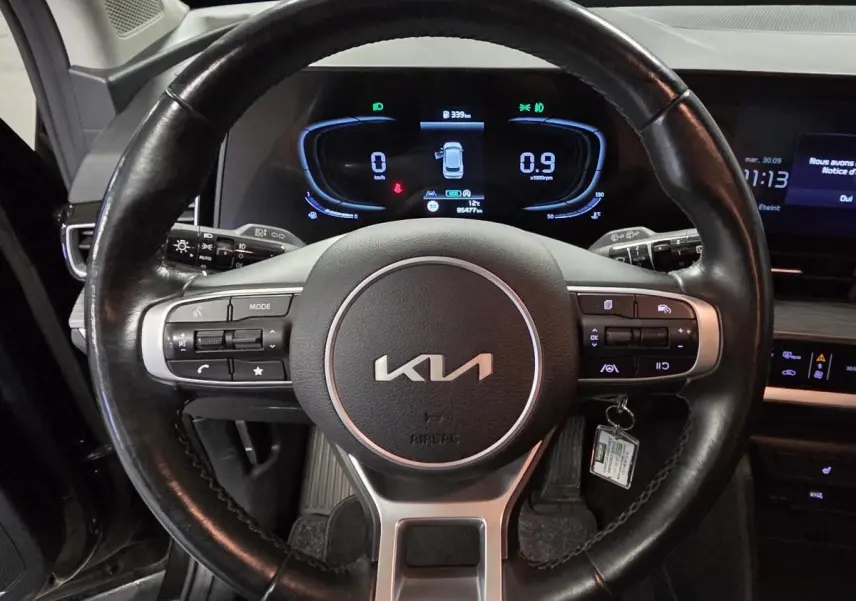 Vue rapprochée du volant cuir noir du Kia Sportage 2022 avec tableau de bord numérique allumé en arrière-plan.