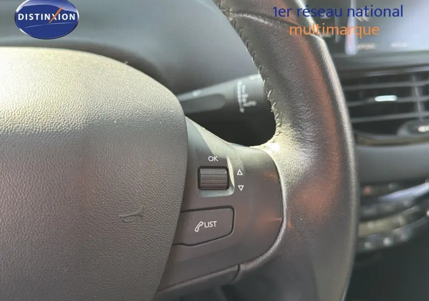 Gros plan sur le volant en cuir noir du Peugeot 2008 gris platinium, avec commandes intégrées et tableau de bord en arrière-plan.