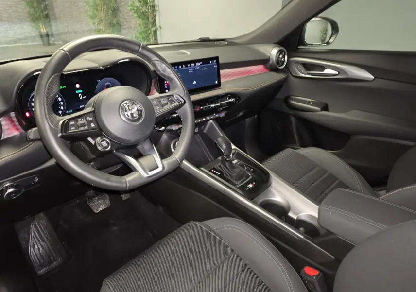 Vue intérieure côté conducteur de l'Alfa Romeo Tonale 1.3 PHEV 2023 avec tableau de bord digital et sellerie noire carbone.
