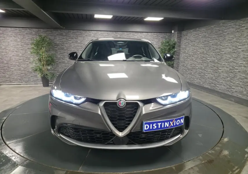 Vue frontale d'une Alfa Romeo Tonale grise métallisée avec phares LED allumés dans un showroom.