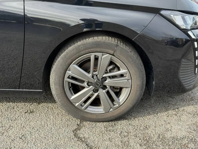 Gros plan sur la roue avant gauche de la Peugeot 308 2024 noire Perla Nera avec jante alliage au design moderne.