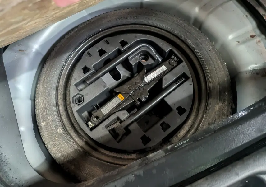 Gros plan sur la roue de secours et le cric dans le coffre d'une Renault Clio V gris platine, version société diesel 2023.