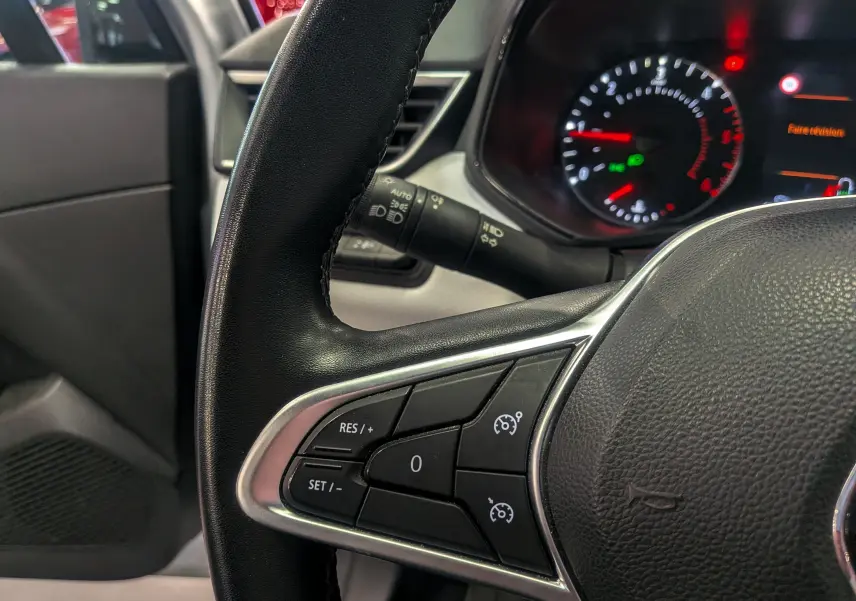Gros plan sur le volant noir de la Renault Clio V gris platine, montrant les commandes de régulateur de vitesse à gauche.