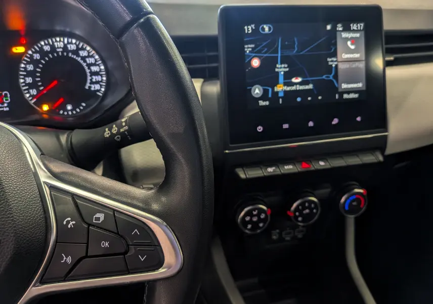Vue intérieure de la Renault Clio V gris platine, tableau de bord avec écran tactile et commandes au volant côté gauche.