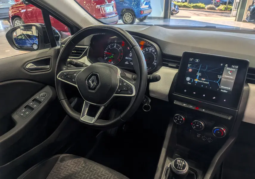 Vue intérieure côté conducteur de la Renault Clio V gris platine, montrant le volant, tableau de bord et écran tactile central.