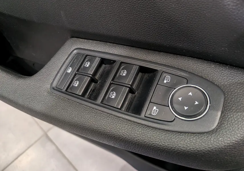 Gros plan sur les commandes électriques des vitres et rétroviseurs côté conducteur d'une Renault Clio V gris platine.