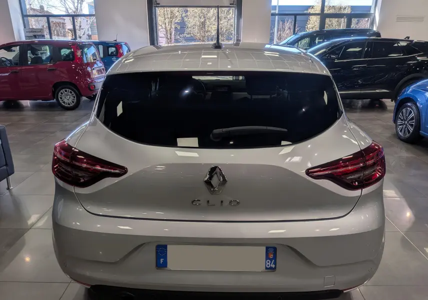 Vue arrière d'une Renault Clio V gris platine dans un showroom, avec feux arrière allongés et vitre arrière teintée.