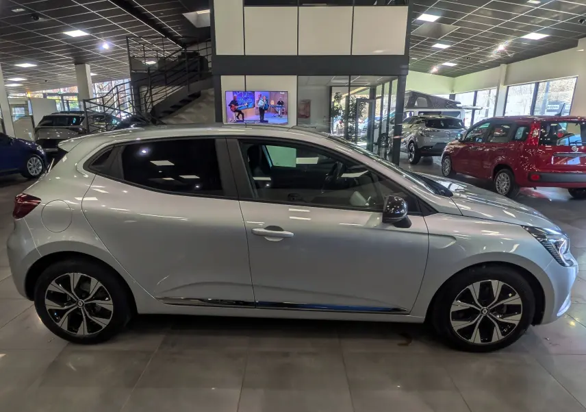 Vue de profil côté gauche d'une Renault Clio V gris platine en showroom, avec jantes bi-ton et vitres teintées.