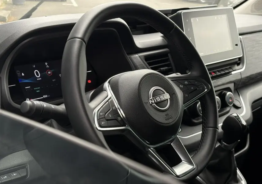 Vue intérieure rapprochée du volant noir et du tableau de bord numérique du Nissan Primastar 2025.