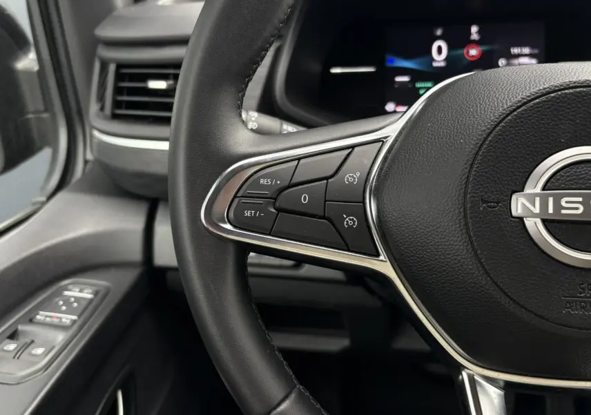 Vue rapprochée du volant noir du Nissan Primastar 2025 avec commandes au volant et tableau de bord numérique en arrière-plan.
