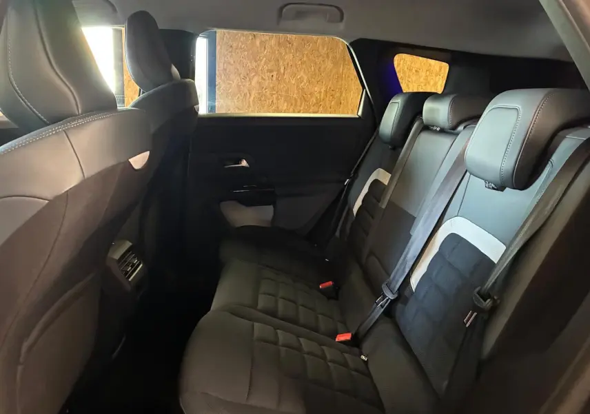 Vue intérieure arrière du Citroën C5 Aircross 1.2 hybride 2026, sièges tissu noir avec détails gris et ceintures visibles.