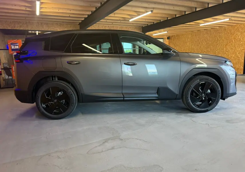 Vue de profil côté gauche d'un Citroën C5 Aircross gris 2026 avec jantes noires dans un garage en bois.