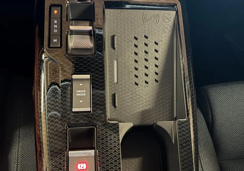 Vue rapprochée de la console centrale noire brillante du Citroën C5 Aircross 1.2 Hybride 145 Plus avec commandes de boîte auto et chargeur sans fil.