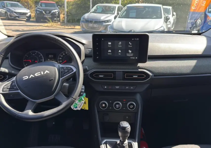 Vue intérieure avant du tableau de bord et volant de la Dacia Sandero 2025, avec écran tactile et levier de vitesse manuel.