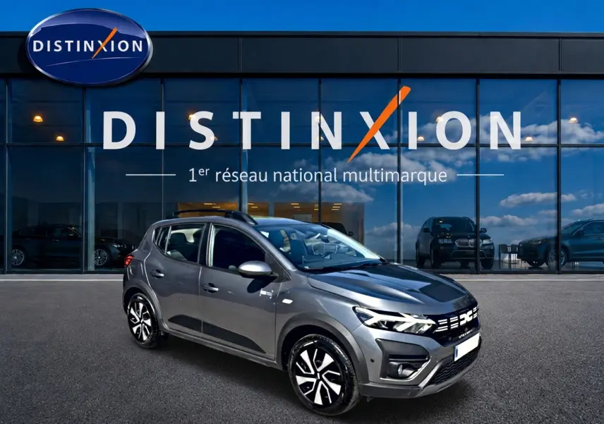 Vue 3/4 avant droit d'une Dacia Sandero Stepway gris schiste avec barres de toit et jantes distinctives.