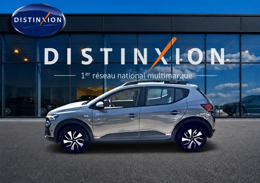 Profil droit de la Dacia Sandero Stepway gris schiste 2025 avec barres de toit et jantes distinctives, devant une vitrine Distinxion.