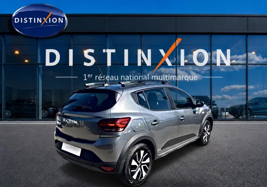 Vue 3/4 arrière droite d'une Dacia Sandero Stepway 2025 gris schiste avec barres de toit et jantes noires.