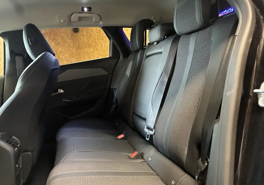 Vue latérale intérieure des sièges arrière noirs en tissu et cuir de la Peugeot 308 SW 2024 avec ceintures attachées.