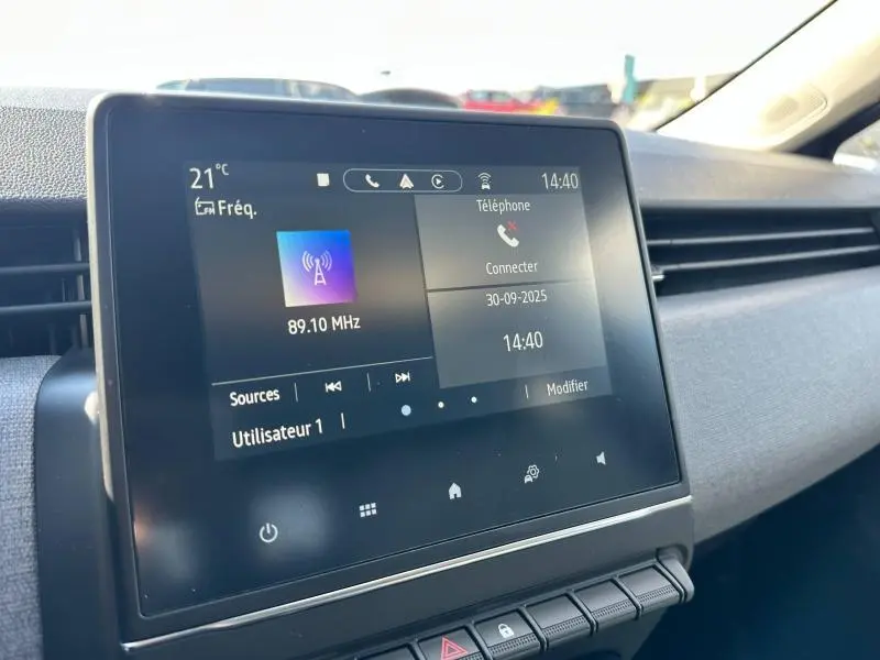 Écran tactile central de la Renault Clio gris Rafale 2025 affichant la radio et la connexion téléphone, vue intérieure côté passager.