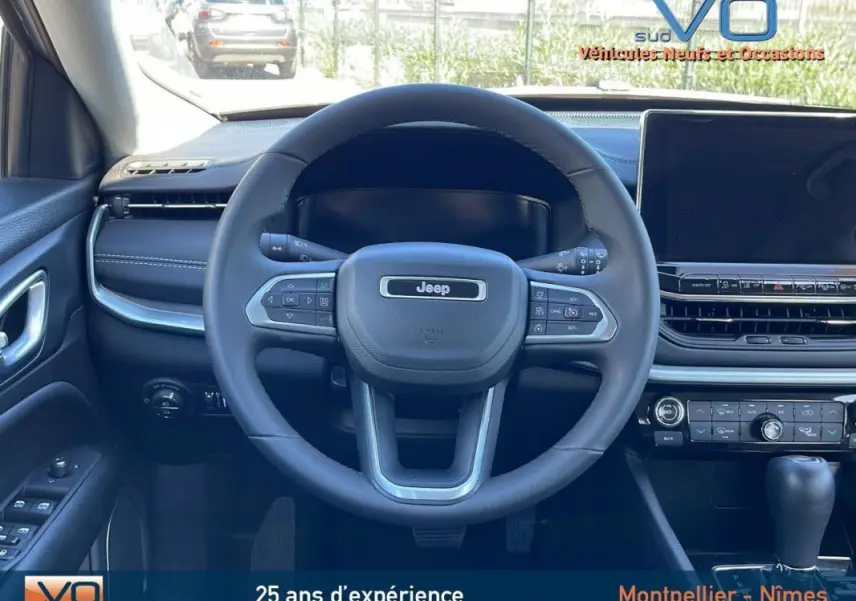 Vue intérieure centrée sur le volant Jeep Compass 2024, tableau de bord noir avec écran tactile et commandes intégrées.