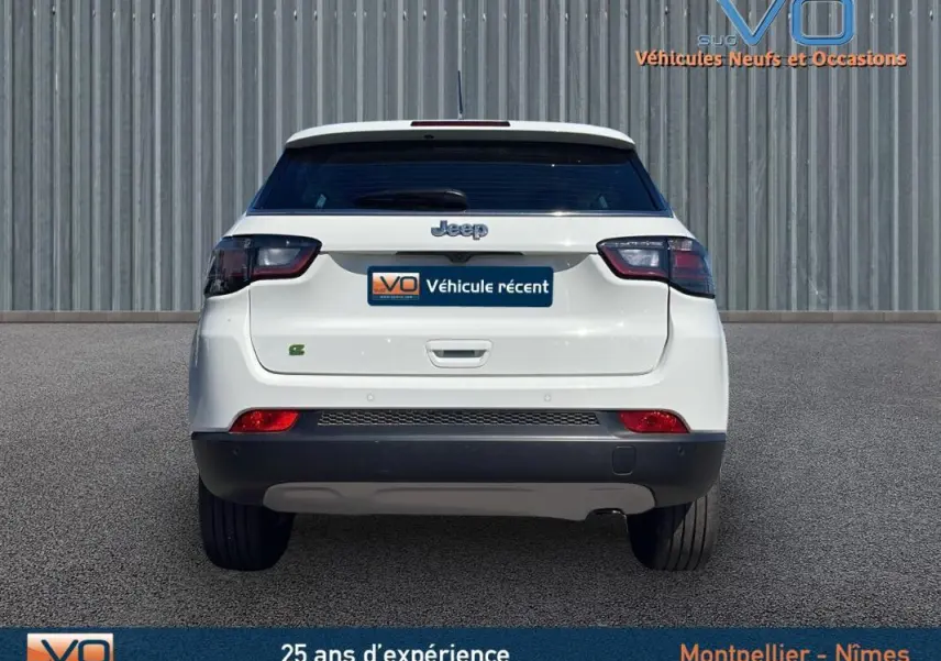 Vue arrière d'un Jeep Compass blanc 2024 avec feux arrière fumés et logo Jeep visible sur fond urbain.